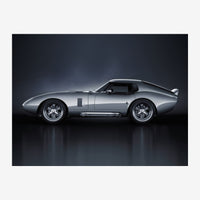 Voiture de sport classique argentée photographiée de profil sur un fond noir, avec son reflet visible au sol.