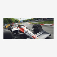 Un monoplace blanc et rouge lancé à grande vitesse sur un circuit automobile, avec des murets de sécurité et des arbres.