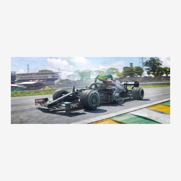 Une monoplace de course noire et turquoise lancée à grande vitesse sur un circuit automobile, avec des stands et des arbres.