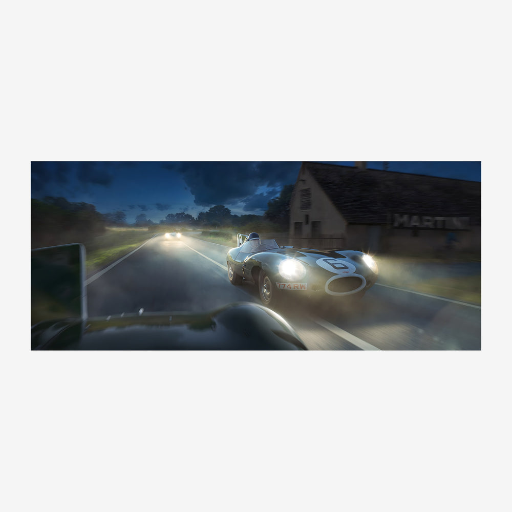 Une voiture de course vintage avec phares allumés fonce sur une route de nuit, passant devant une maison sombre en.
