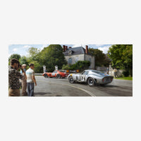 Deux voitures de course vintage, une rouge et une argent numérotées, passent devant un château entouré de verdure, sous le.
