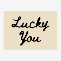 Affiche avec le texte « Lucky You » écrit en cursive noire sur fond beige clair.