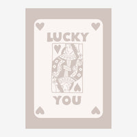 Affiche portrait avec une reine de cœur stylisée au centre, encadrée de cœurs et du texte "LUCKY YOU" sur fond beige et gris.