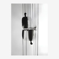 Composition minimaliste montrant une figure humaine noire suspendue à plusieurs fils verticaux sur fond gris et blanc.