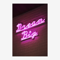 Enseigne lumineuse rose fluo « Dream Big » écrite en lettres cursives néon sur un mur de briques sombres.
