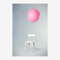 Une chaise blanche en bois retient un ballon rose attaché par un fil fin, sur fond gris dégradé et épuré.