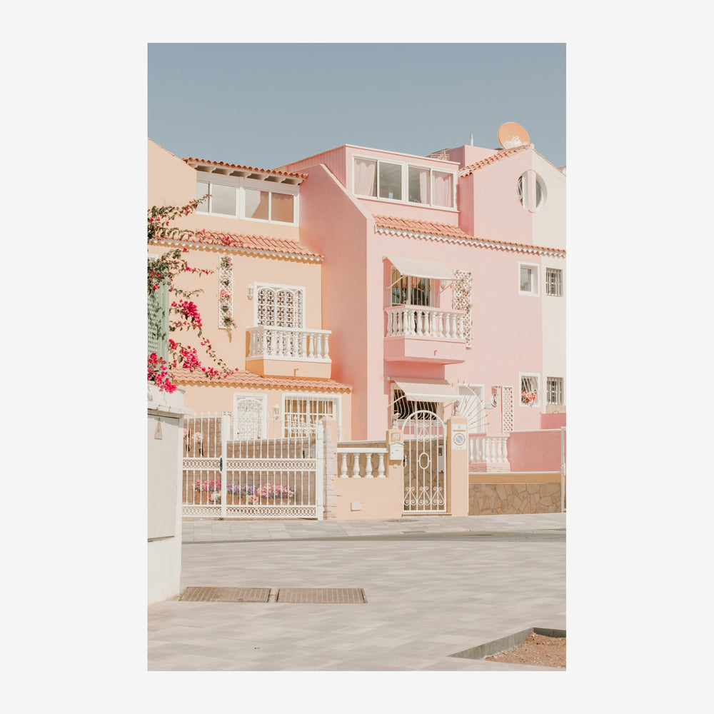 Façade d'une maison rose et crème avec terrasses blanches, toits de tuiles orangées et fleurs rouges grimpantes, sous un.