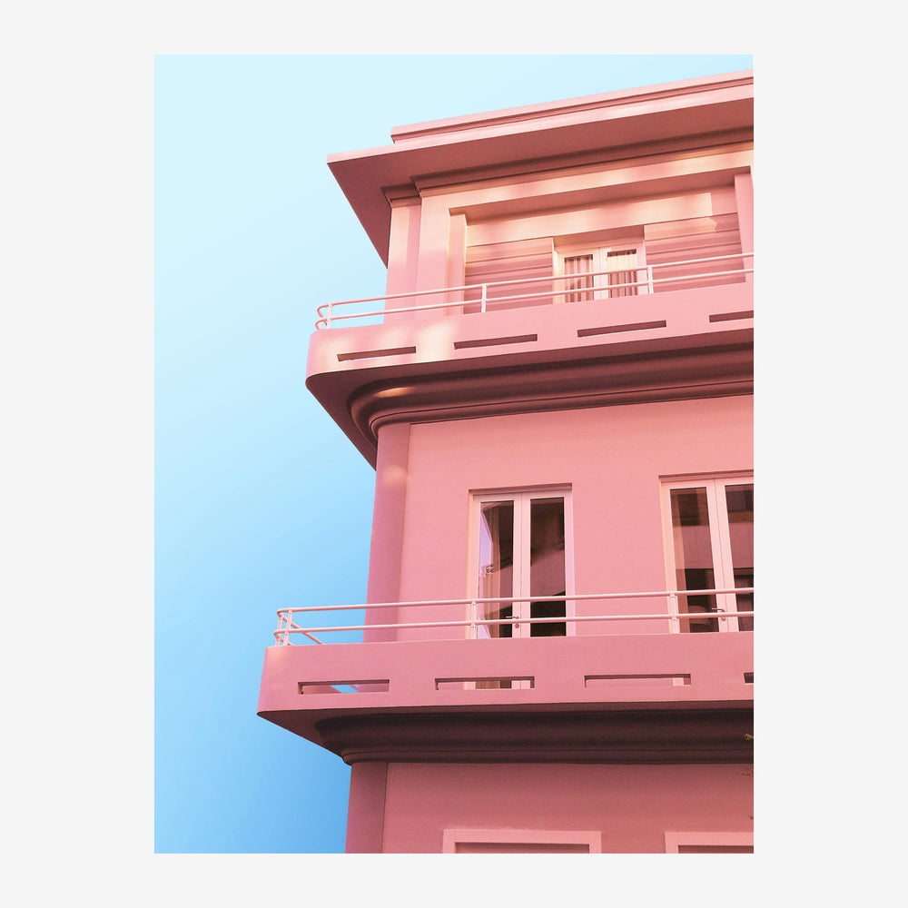 Détail d'une façade de bâtiment rose clair avec balcons et rampes blanc crème, cadré contre un ciel bleu pâle.
