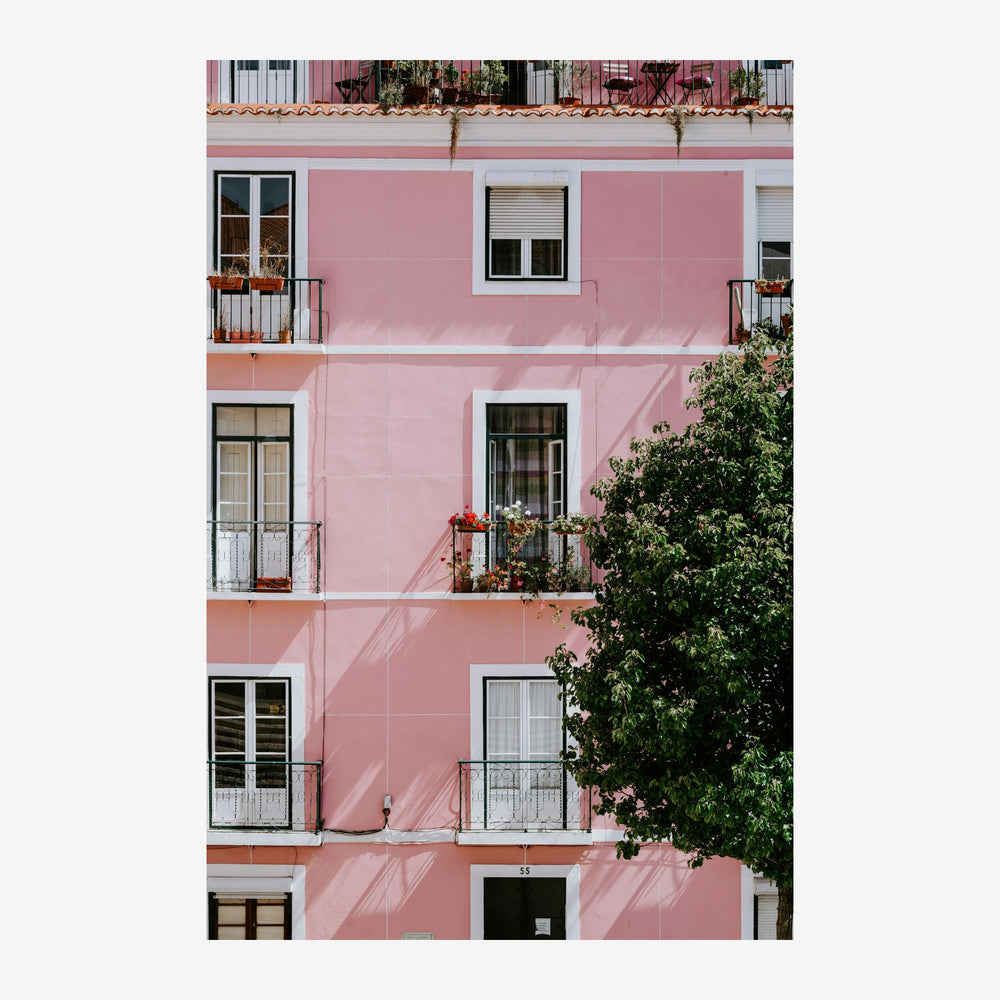 Façade d'immeuble rose pastel avec fenêtres et balcons, lierre vert grimpant sur le côté droit.