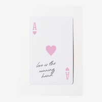 Carte blanche ornée d'un cœur rose au centre, avec des symboles de cartes aux quatre coins et le texte manuscrit « love is.