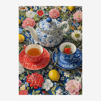 Une théière blanche à décor bleu et blanc, deux tasses de thé assorties en rouge et bleu, des citrons et une fraise.