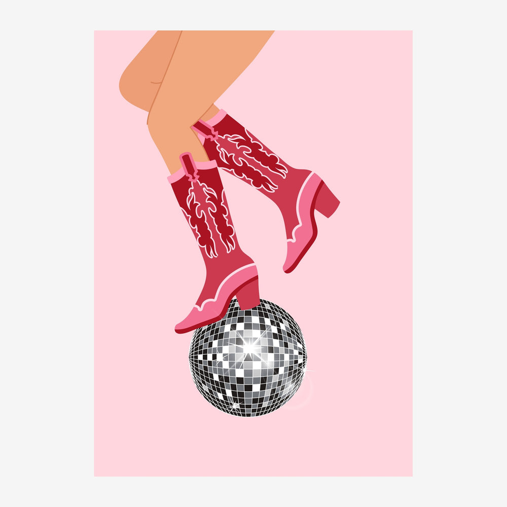 Une paire de bottes de cowboy roses avec motifs blancs posée sur une boule disco noire et blanche, sur fond rose clair.