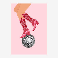 Une paire de bottes de cowboy roses avec motifs blancs posée sur une boule disco noire et blanche, sur fond rose clair.
