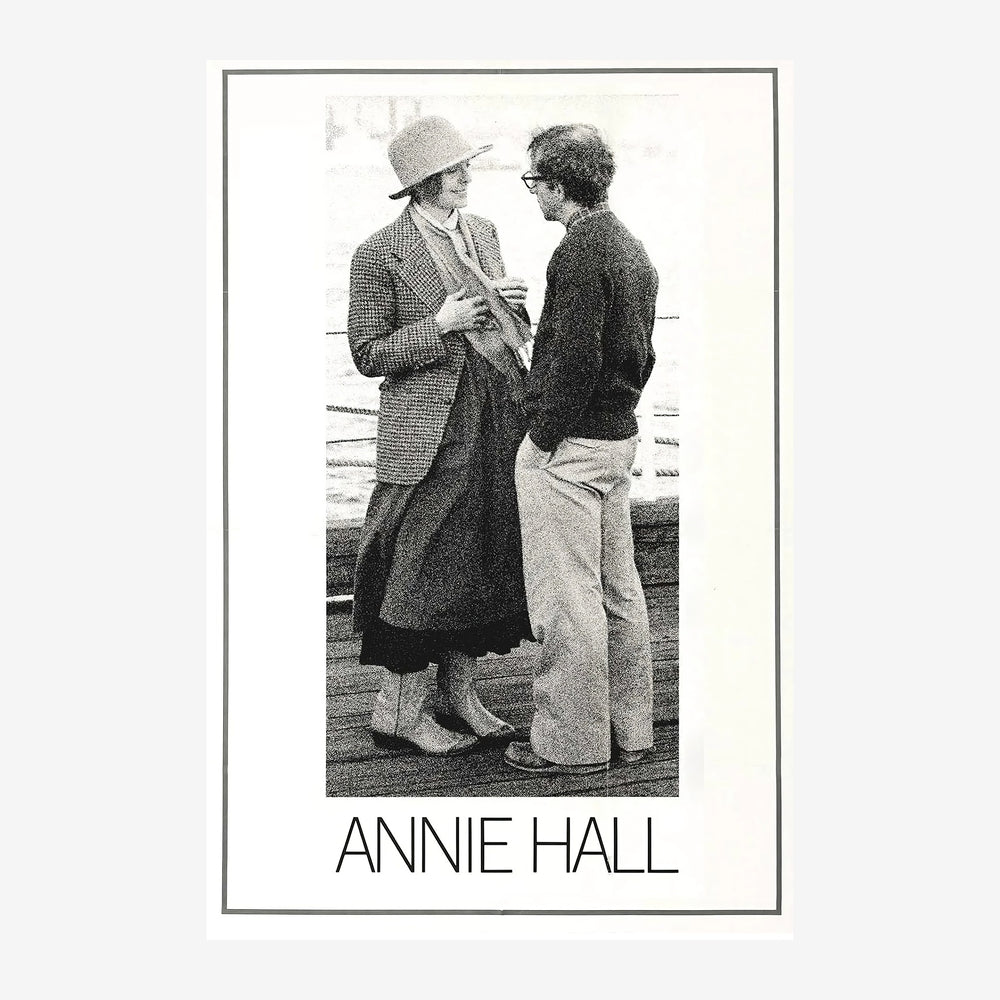 Photographie en noir et blanc de deux femmes se parlant près d'une barrière, l'une portant un chapeau et un blazer, l'autre.