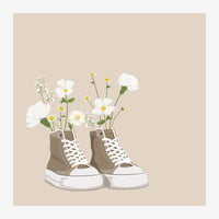 Deux baskets en toile beige et blanc avec lacets blancs, remplies d'un bouquet de marguerites blanches et jaunes avec tiges.